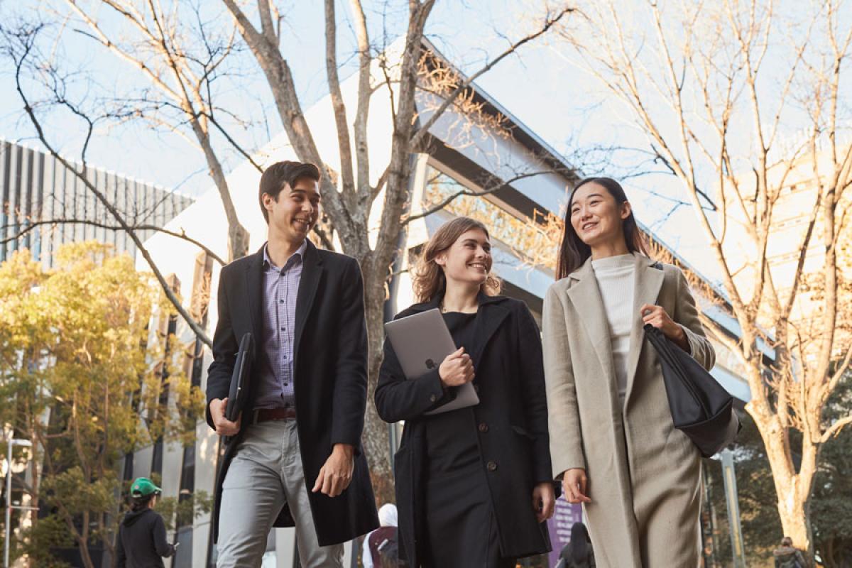 图为，3名身穿商务装的学生在校园外散步，边走边微笑。