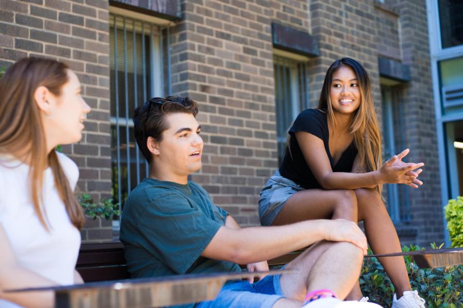 三名学生坐在肯斯大学主校区室外的长凳上。